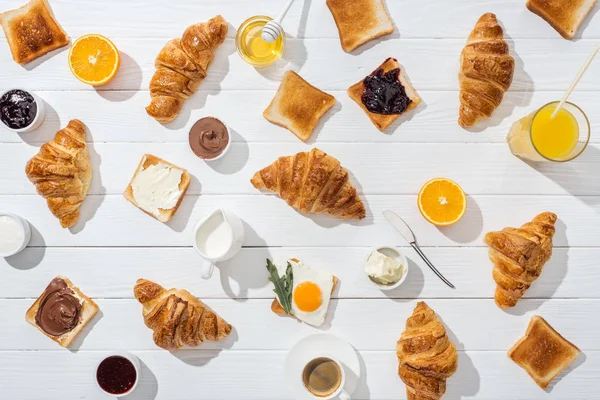 Blick von oben auf süße Croissants in der Nähe von leckeren Toasts und Getränken auf Weiß — Stockfoto