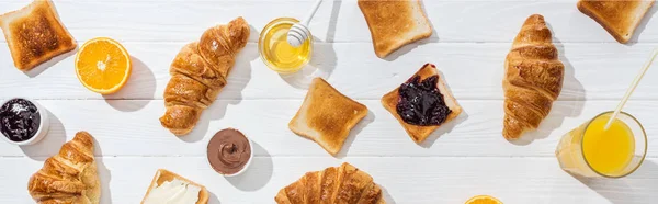 Panoramic shot of sweet croissants near tasty toasts and orange juice on white — Stock Photo