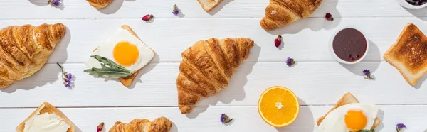 Colpo panoramico di dolci croissant e gustosi toast vicino a fiori secchi su bianco — Foto stock