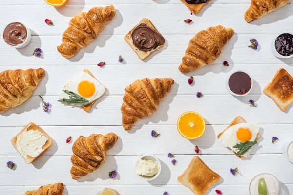 Top view of sweet croissants and tasty toasts with arugula leaves on friend eggs near dried flowers on white — Stock Photo