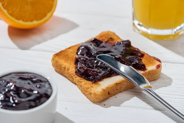 Selective focus of toast with jam near knife and half of orange on white — Stock Photo