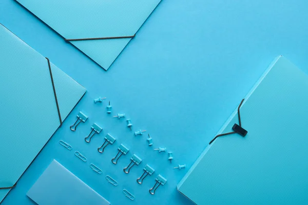 Colocação plana de pastas de papel e vários artigos de papelaria isolados em azul — Fotografia de Stock