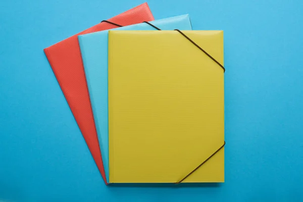 Vista superior de ligantes de papel vermelho, azul e amarelo isolados em azul — Fotografia de Stock