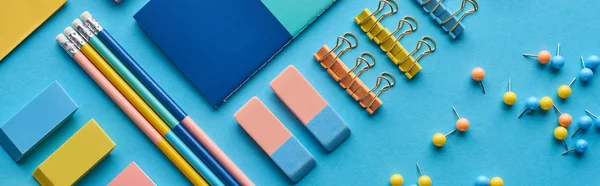 Plano panorámico de lápices, alfileres y papelería de colores aislados en azul - foto de stock