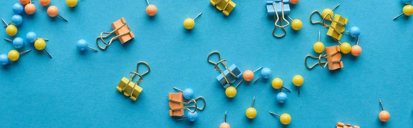 Panoramic shot of colorful scattered push pins and paper clips isolated on blue — Stock Photo