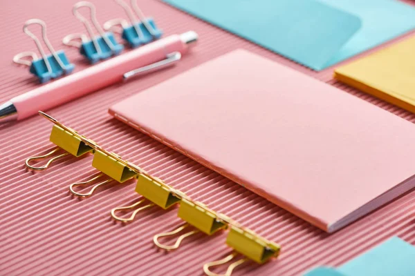 Carnet, trombones et fournitures de papeterie colorées sur rose — Photo de stock