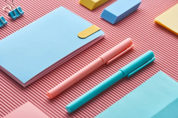 Colorful pens, notebooks and erasers on pink — Stock Photo