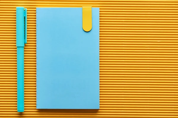 Vista superior de la pluma azul y el cuaderno en amarillo con espacio de copia - foto de stock