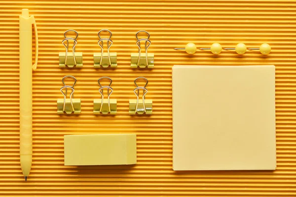 Vista superior da caneta, clipes de papel e suprimentos de papelaria de escritório arranjados coloridos em amarelo — Fotografia de Stock
