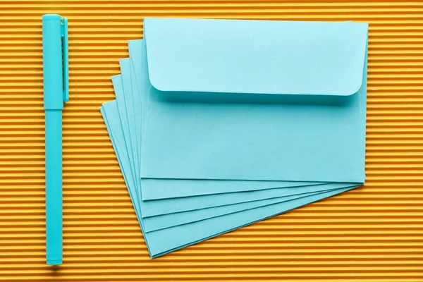Вид зверху на ручку і сині конверти на жовтому — стокове фото