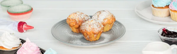 Plano panorámico de deliciosos muffins y cupcakes en mesa de madera blanca - foto de stock