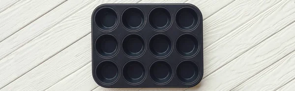 Panoramic shot of metal muffin tray on white wooden table — Stock Photo