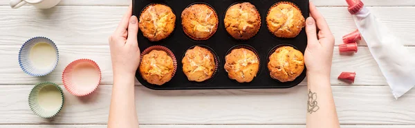 Plan panoramique de la femme tenant une boîte de cuisson avec des cupcakes sur la table avec des outils de cuisson — Photo de stock