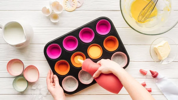 Vista cortada da mulher derramando massa líquida na panela de cupcake na mesa — Stock Photo