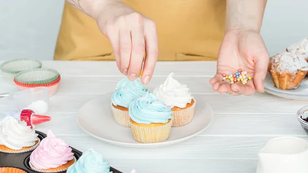 Abgeschnittene Ansicht einer Frau, die Cupcakes mit Streusel dekoriert — Stockfoto