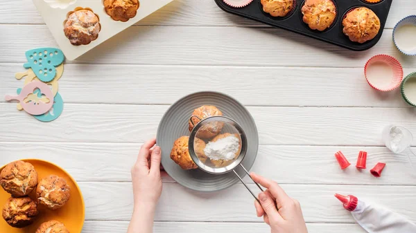 Visão parcial da mulher que decora cupcakes com açúcar em pó na mesa com ferramentas de cozimento — Fotografia de Stock