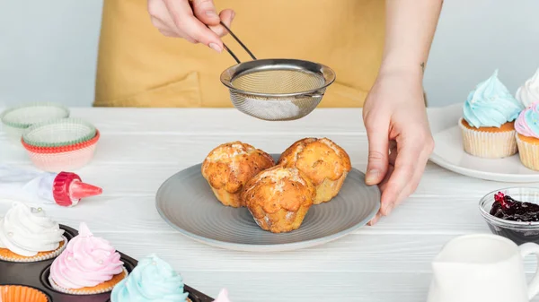 Partial view of woman decorating cupcakes with powdered sugar isolated on grey — Stock Photo