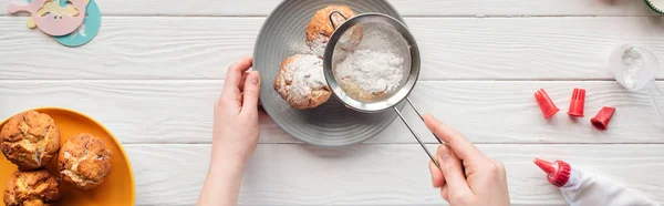 Tiro panorámico de mujer decorando cupcakes con azúcar en polvo en la mesa blanca - foto de stock