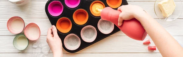 Panoramic shot of woman pouring liquid dough in cupcake pan on table — Stock Photo