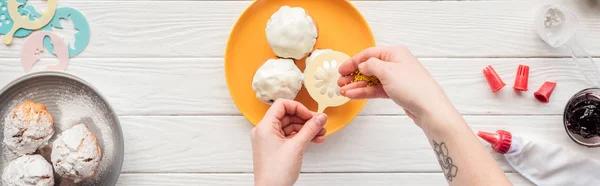 Panoramic shot of woman decorating cupcakes with baking stencil and sprinkles — Stock Photo