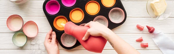 Panoramic shot of woman pouring liquid dough in cupcake pan on table — Stock Photo