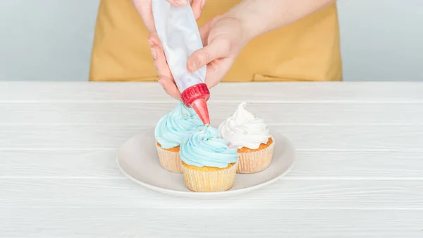 Cropped view of woman decorating cupcakes with icing bag — Stock Photo