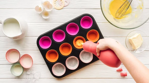 Abgeschnittene Ansicht einer Frau, die flüssigen Teig in Cupcake-Pfanne auf den Tisch gießt — Stockfoto