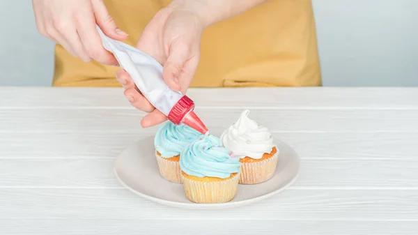 Abgeschnittene Ansicht einer Frau, die Cupcakes mit Zuckerguss verziert — Stockfoto