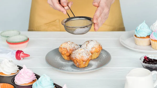 Cropped view of woman decorating cupcakes with powdered sugar isolated on grey — Stock Photo