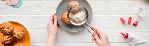 Panoramic shot of woman decorating cupcakes with powdered sugar and sieve on white table — Stock Photo