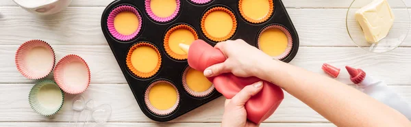 Panoramic shot of woman pouring liquid dough in muffin mold on table — Stock Photo