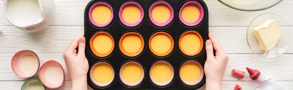 Panoramic shot of woman holding muffin mold with liquid dough on table with ingredients — Stock Photo