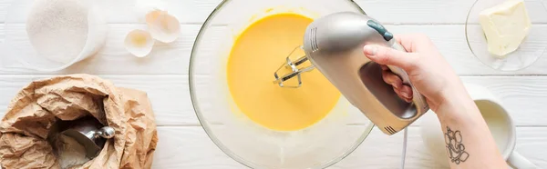 Panoramic shot of woman mixing dough with hand mixer on wooden table — Stock Photo