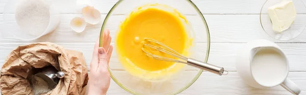 Panoramic shot of woman holding bowl with balloon whisk and liquid dough on table — Stock Photo