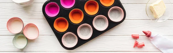 Panoramic shot of muffin mold, butter, paper forms and icing bag on table — Stock Photo