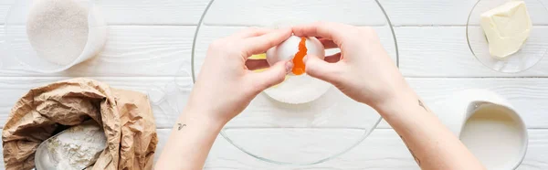 Plan panoramique de femme craquant oeuf dans un bol tout en cuisinant sur la table — Photo de stock