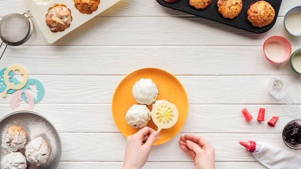 Ausschnitt einer Frau beim Dekorieren von Cupcakes mit Schablone auf dem Tisch mit Backwerkzeugen — Stockfoto