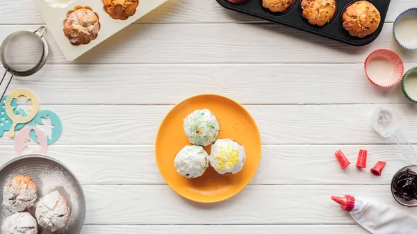 Vue de dessus de délicieux cupcakes et outils de cuisson sur table en bois blanc — Photo de stock