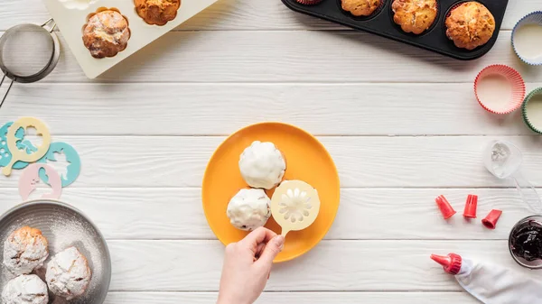 Ausschnitt einer Frau beim Dekorieren von Cupcakes mit Schablone auf dem Tisch mit Backwerkzeugen — Stockfoto