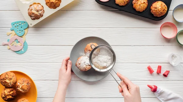 Cropped view of woman decorating cupcakes with powdered sugar on white table — Stock Photo