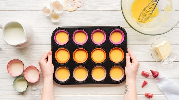 Vista ritagliata della donna che tiene muffin stampo con pasta liquida sul tavolo con ingredienti — Foto stock