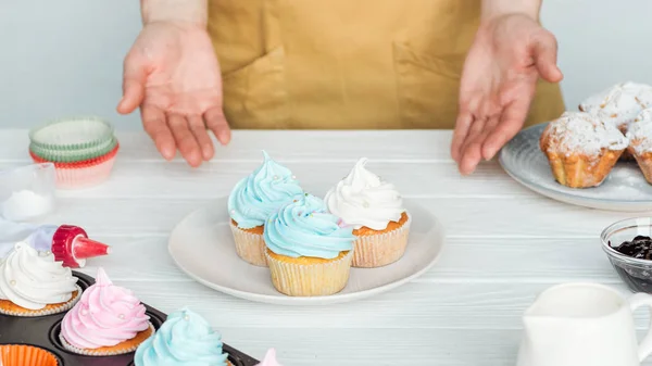 Cropped view of woman Gesturing near plate with cupcakes on table isolated on grey — Stock Photo