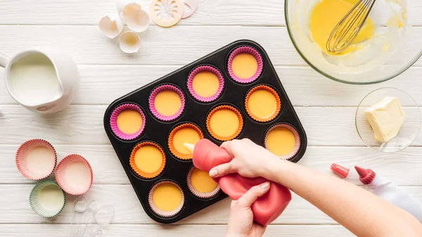 Teilansicht einer Frau, die flüssigen Teig in Muffinform auf den Tisch gießt — Stockfoto