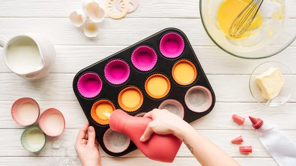 Vue recadrée de la femme versant la pâte liquide dans le moule à muffins sur la table — Photo de stock