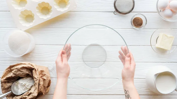 Ausgeschnittene Ansicht einer Frau, die eine Glasschale mit Küchenutensilien und Zutaten auf dem Tisch hält — Stockfoto