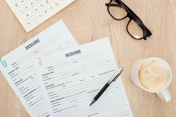 Draufsicht auf Brille, Stift, Taschenrechner, Tasse Cappuccino und Lebenslauf-Vorlagen auf Holzoberfläche — Stockfoto