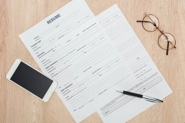 Vista superior de gafas, bolígrafo, smartphone con pantalla en blanco y plantilla de CV en superficie de madera - foto de stock