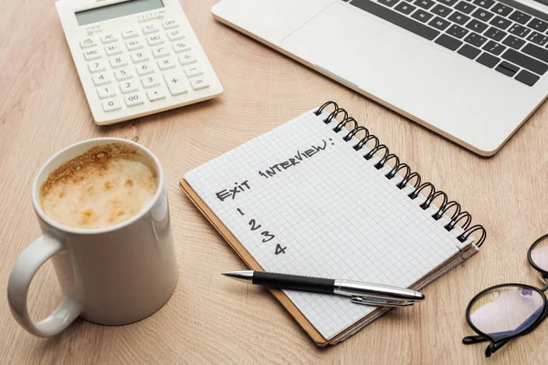 Notebook com letras de entrevista de saída e números em mesa de madeira com laptop, artigos de papelaria, óculos e xícara de café — Fotografia de Stock