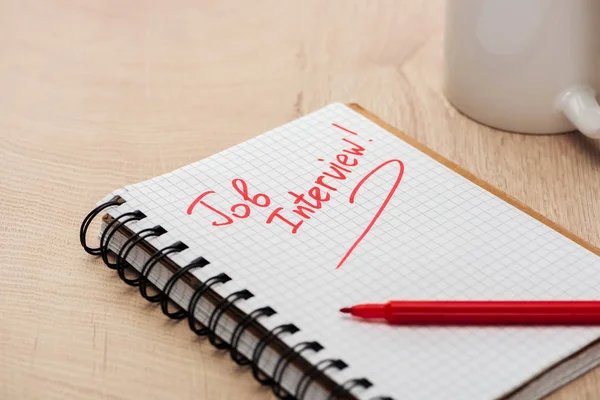 Notebook com entrevista de emprego lettering em mesa de madeira com marcador vermelho e copo — Fotografia de Stock