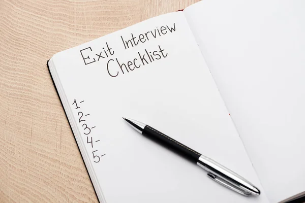 Notebook with pen, exit interview checklist lettering and numbers on wooden table — Stock Photo